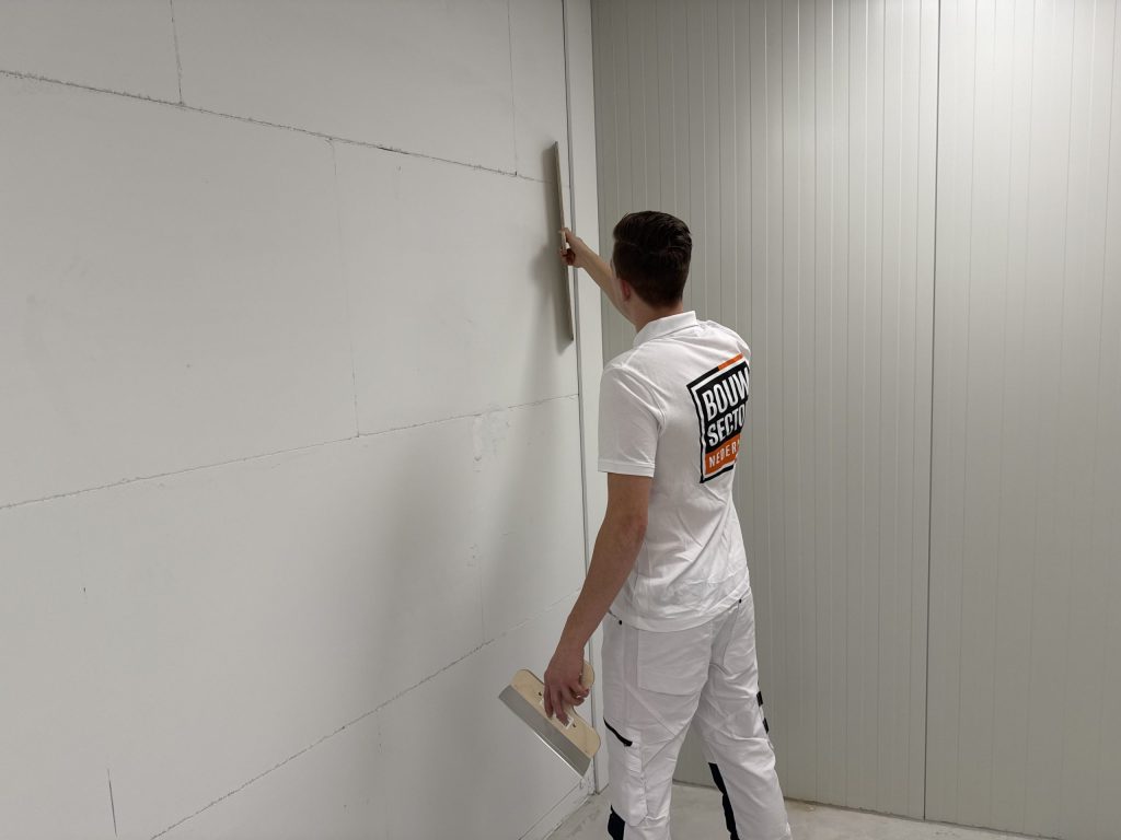 Vakman van Bouwsector Nederland schuurt een wand glad met een schuurbord op een steel