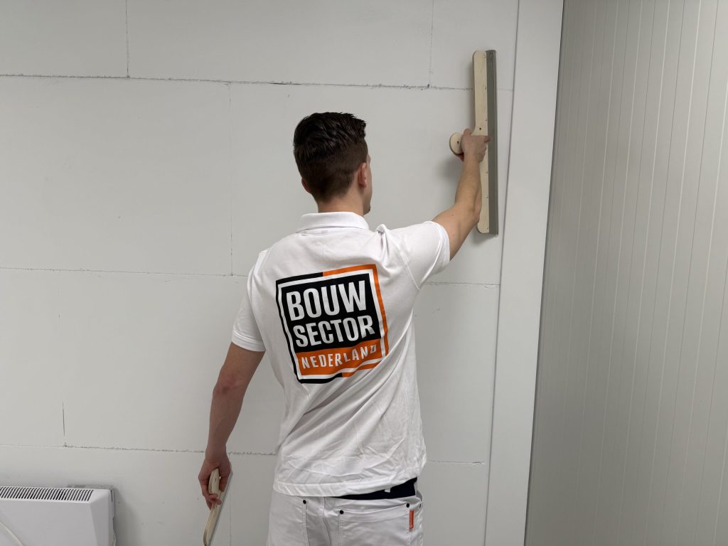 Vakman van Bouwsector Nederland werkt met een brede spaan een naad in de wand af