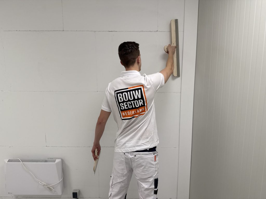 Vakman van Bouwsector Nederland trekt met een brede spaan een wand vlak
